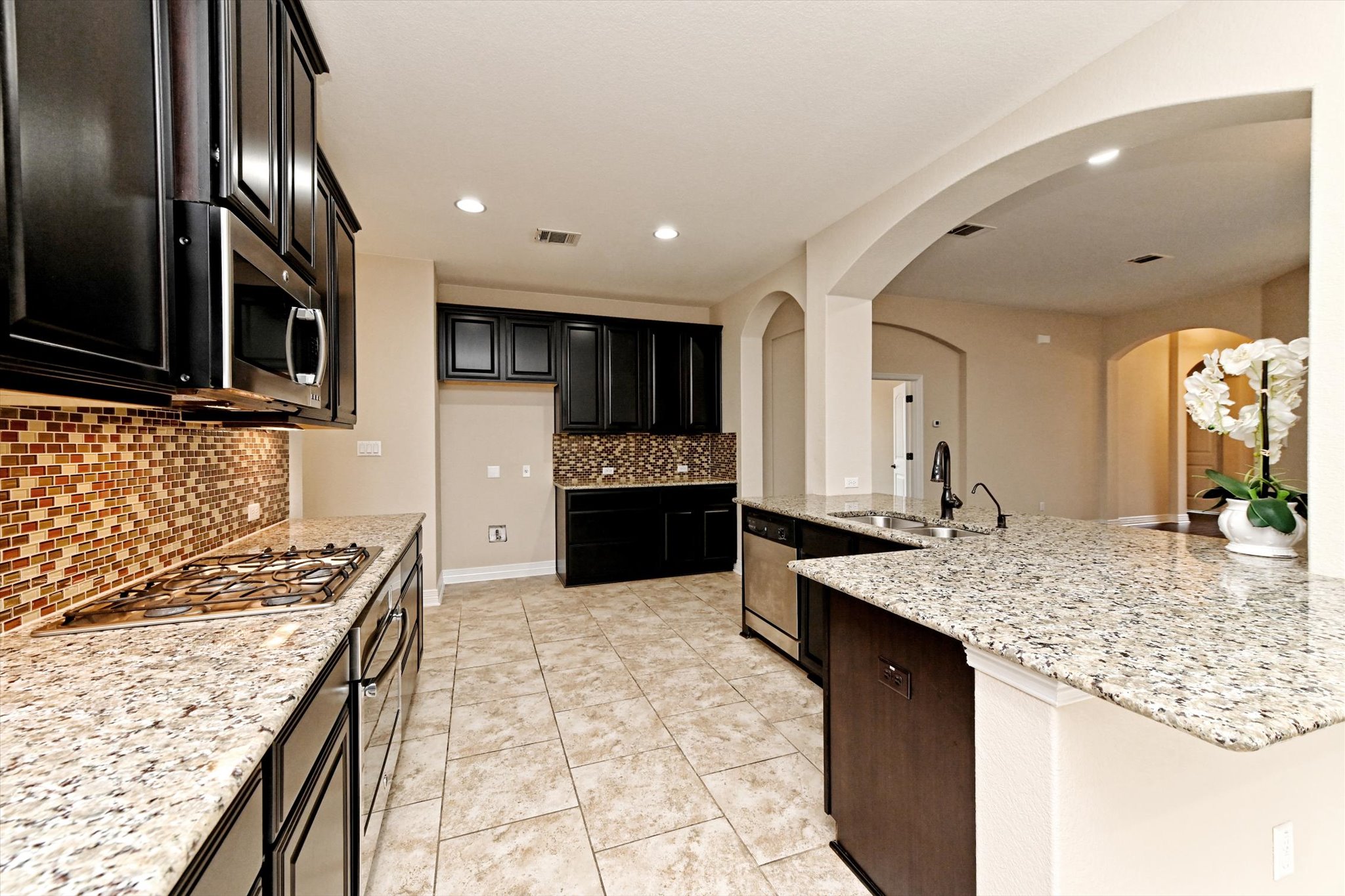 18500 Rio Chama Lane Austin, TX 78738 - Photo 9 of 28 Kitchen featuring dark wood cabinetry, granite countertops, a built-in stainless steel microwave, and a gas stovetop