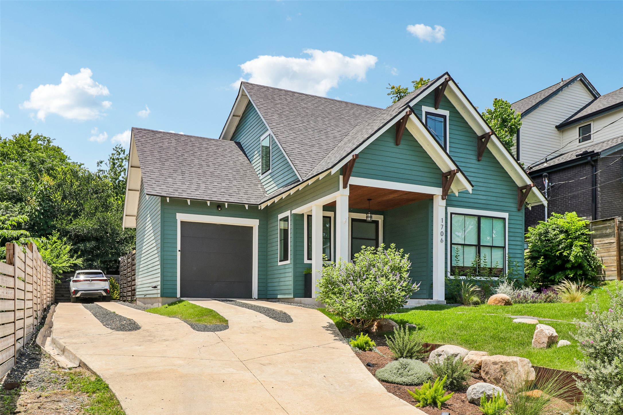 1706 Perez Street, Unit 1 Austin, TX 78721 - Photo 2 of 36 A charming teal residence showcases a neatly manicured lawn, a concrete driveway leading to the attached garage, and a covered front entry.