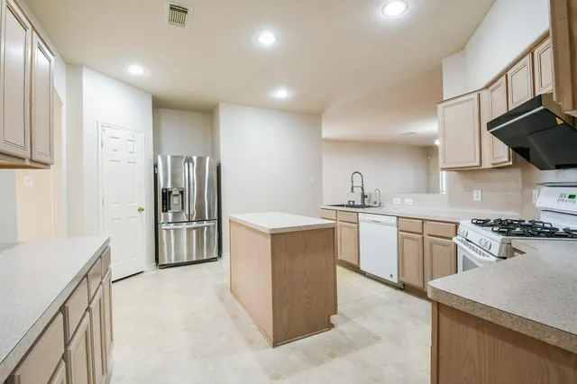 a kitchen with stainless steel appliances kitchen island granite countertop a refrigerator a sink a stove and white cabinets