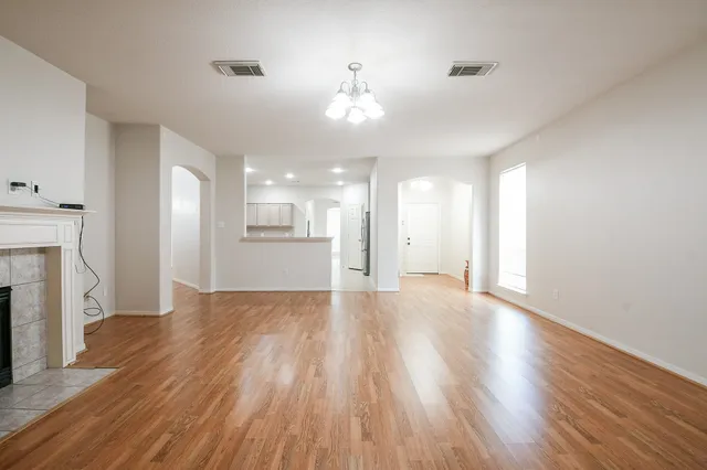 a view of an empty room with wooden floor and a kitchen