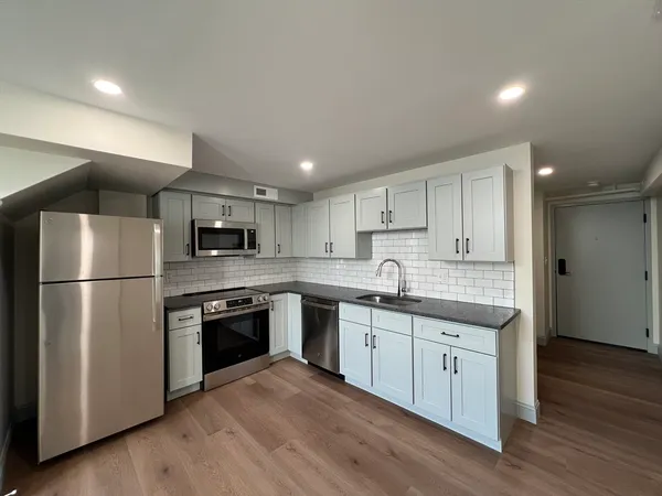 a kitchen with stainless steel appliances granite countertop a refrigerator a sink dishwasher a stove top oven a refrigerator and white cabinets with wooden floor