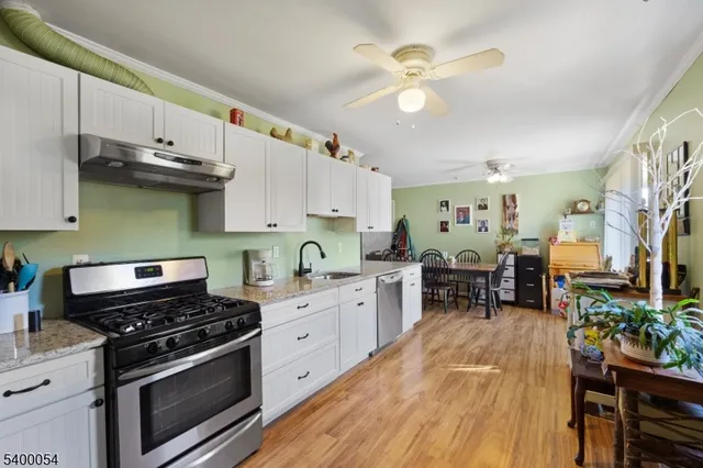 a kitchen with stainless steel appliances a stove a sink dishwasher and white cabinets with wooden floor