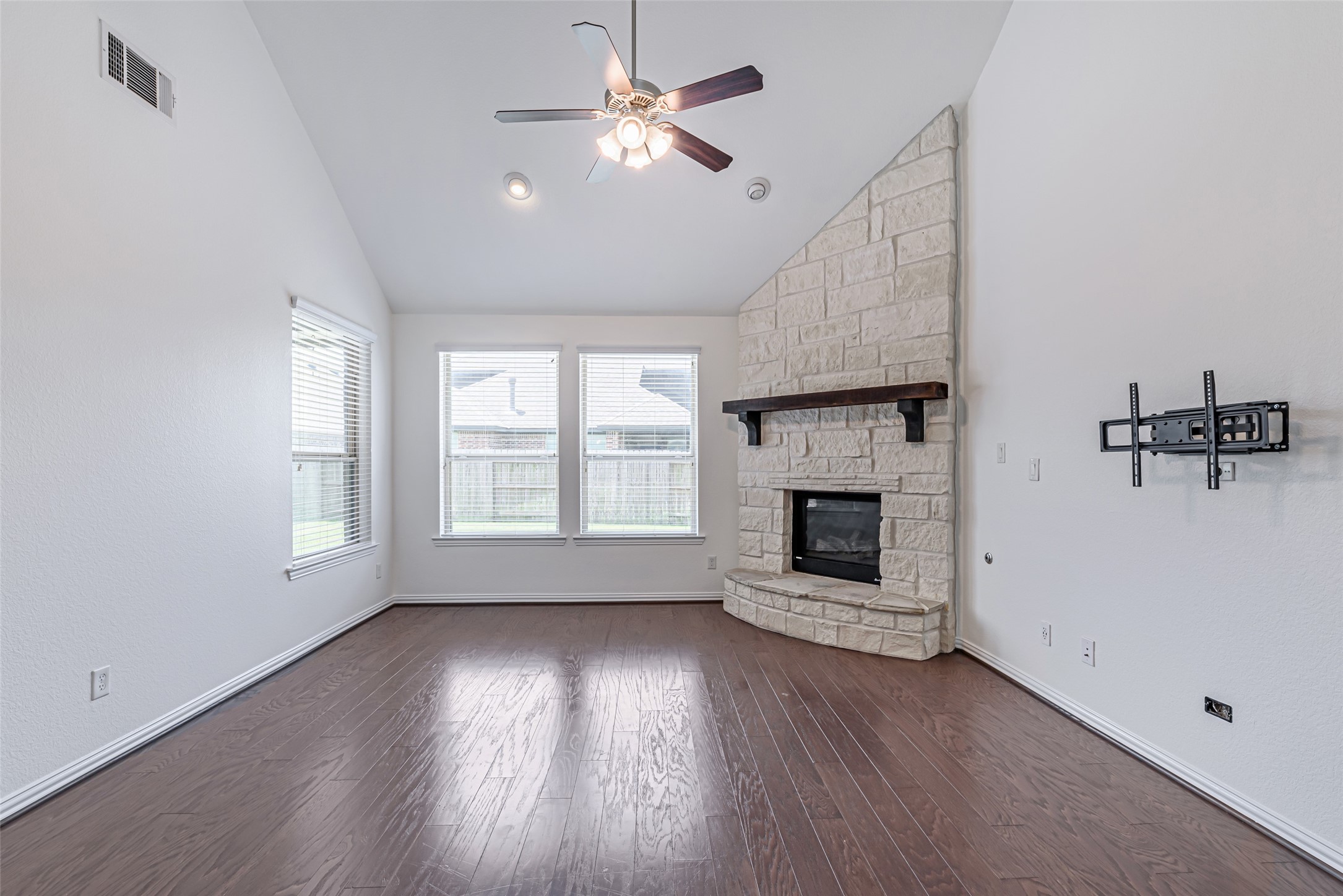 23635 Kingston Ridge Way Katy, TX 77493 - Photo 13 of 36 This bright living room features vaulted ceilings, and large windows for natural light. It includes a stone gas log fireplace with a wooden mantel and hardwood floors, ideal for cozy gatherings.