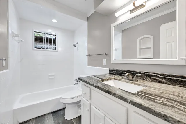 a bathroom with a granite countertop sink a toilet a mirror and bathtub