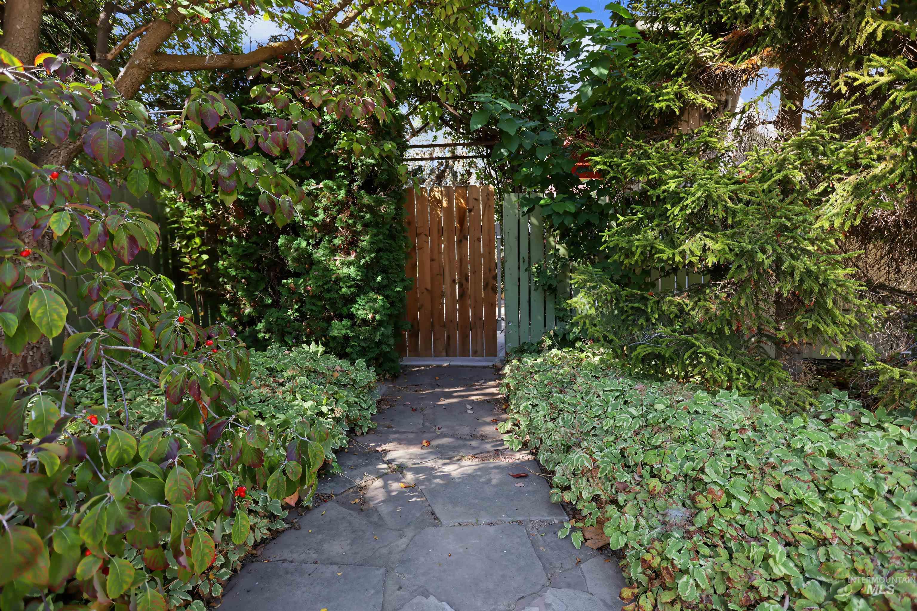 508 East Elm Avenue Parma, ID 83660 - Photo 36 of 50 Stone paver pathway leading to a wood privacy gate, flanked by mature trees and lush ground cover