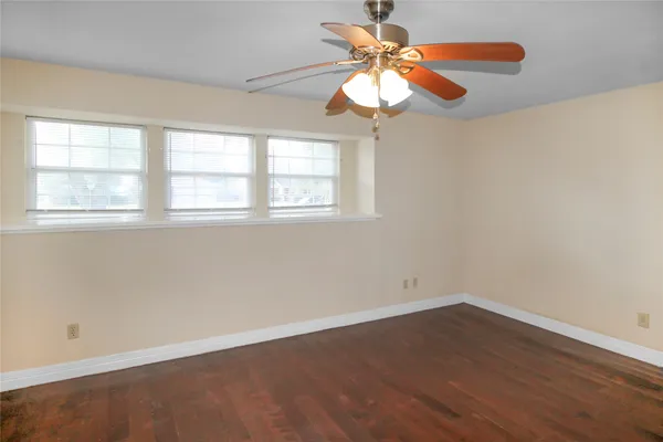 an empty room with wooden floor fan and windows