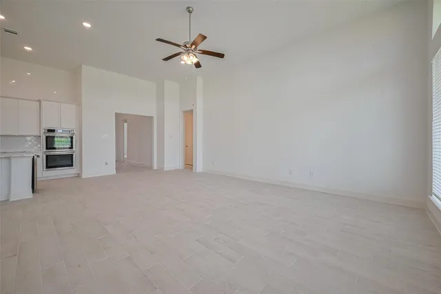 an empty room with chandelier fan and windows