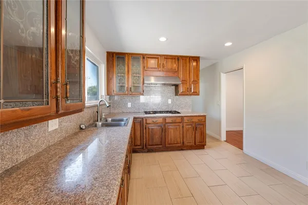 a large white kitchen with granite countertop a sink and dishwasher a stove with wooden floor