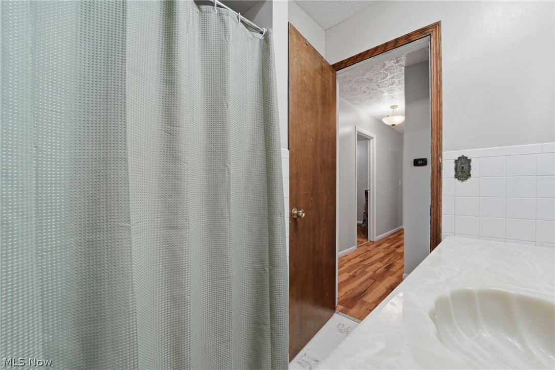 14557 Ellsworth Road Berlin Center, OH 44401 - Photo 18 of 23 Full bath featuring a shower with shower curtain, a textured ceiling, vanity, tile walls, and wood finished floors