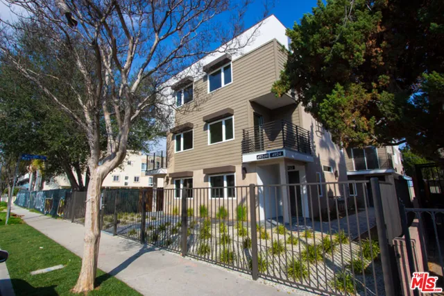 a view of a brick house with a small yard plants and large trees