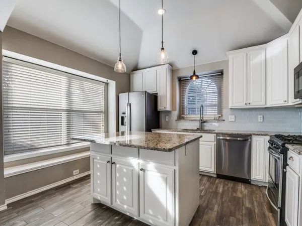 a kitchen with stainless steel appliances granite countertop a sink a stove a refrigerator and island with wooden floor