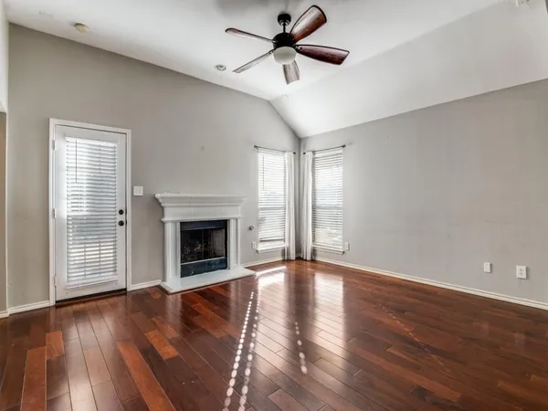 a view of an empty room with wooden floor fireplace and a window