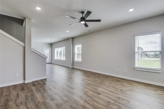 an empty room with wooden floor fan and windows