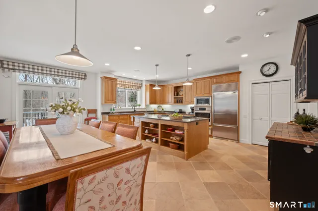a kitchen with stainless steel appliances kitchen island granite countertop a stove a refrigerator a sink a oven and a dining table with the view of living room