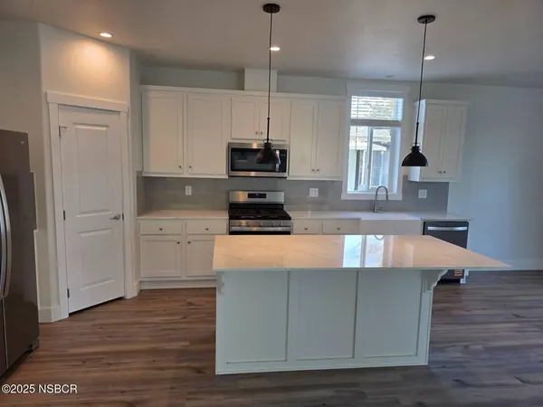 a kitchen with kitchen island granite countertop a stove a sink a refrigerator and white cabinets with wooden floor