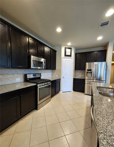 a large kitchen with stainless steel appliances wooden cabinets a stove a sink and a microwave
