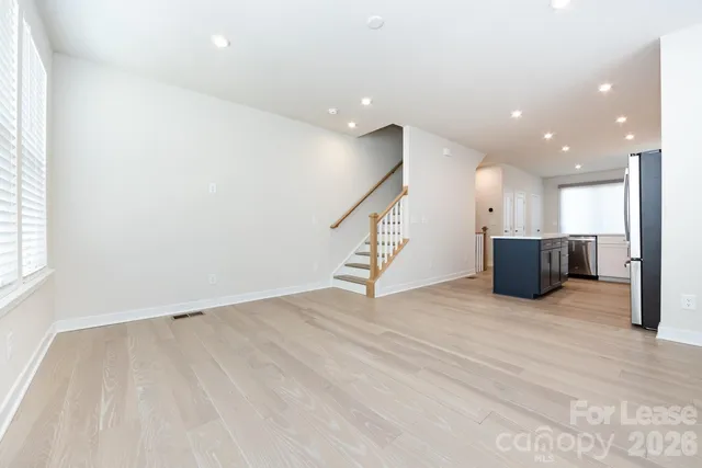 an empty room with wooden floor and kitchen view