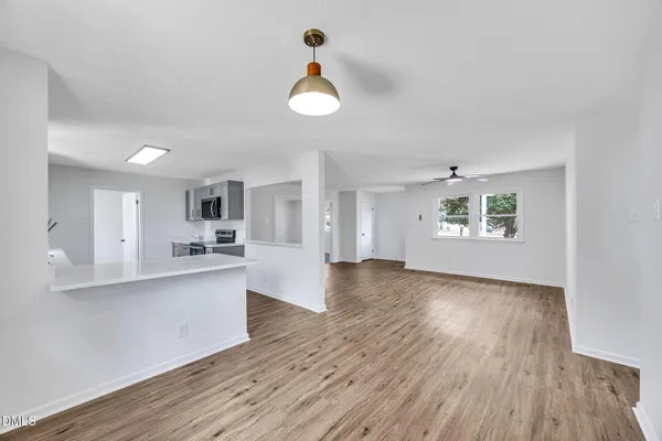 a view of a kitchen and an empty room with wooden floor and a kitchen