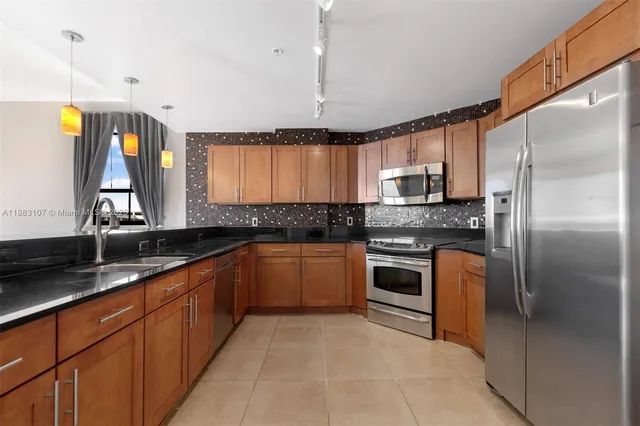 a large kitchen with granite countertop a refrigerator a sink a stove a microwave a counter top space and cabinets