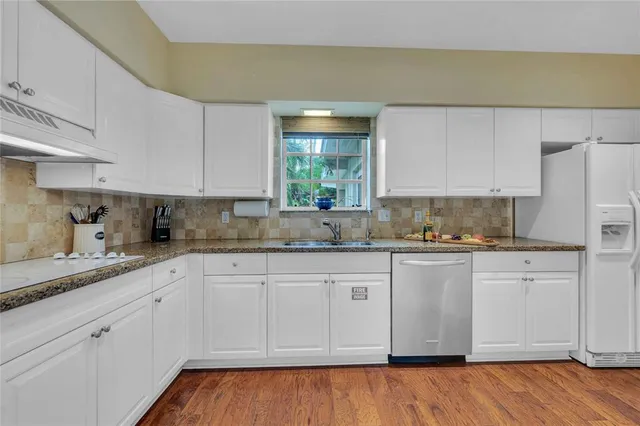 a kitchen with granite countertop white cabinets white appliances a sink and dishwasher