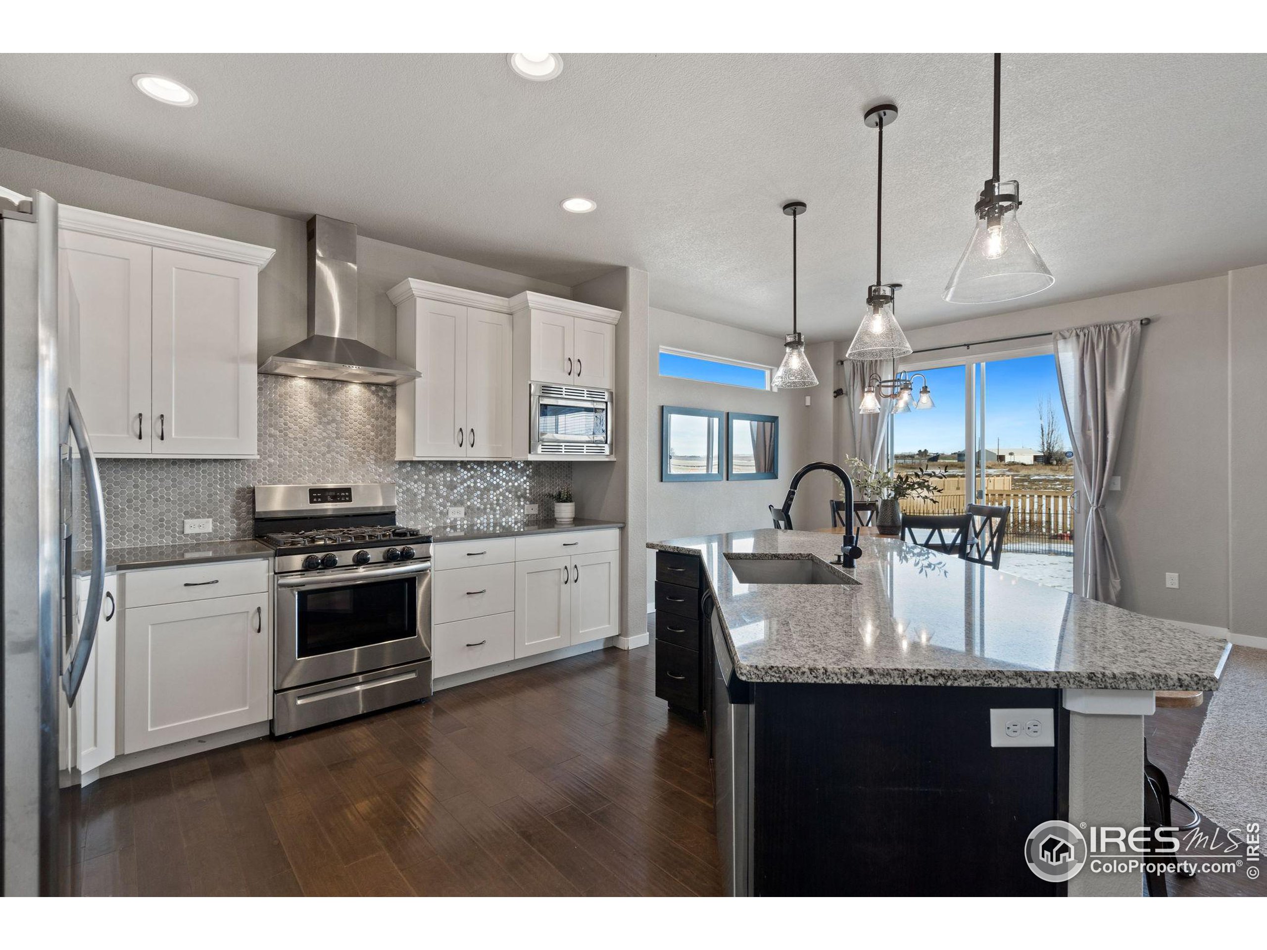a kitchen with kitchen island granite countertop a stove a sink dishwasher and white cabinets with wooden floor