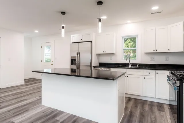 a kitchen with stainless steel appliances granite countertop a refrigerator a sink dishwasher a stove and white countertops with wooden floor