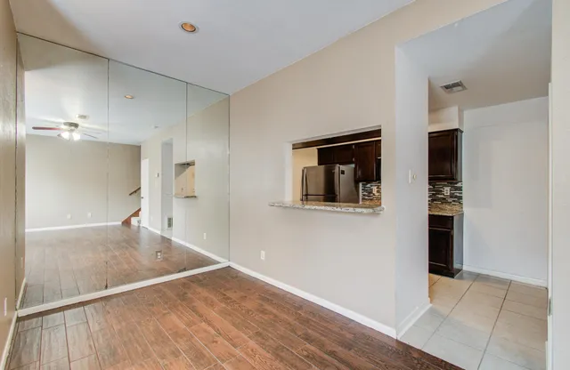a view of a hallway to an empty room with wooden floor and a kitchen