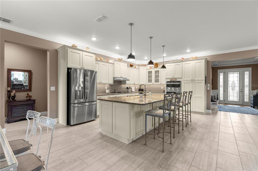 9099 Southwest 89th Loop Ocala, FL 34481 - Photo 18 of 66 a kitchen with stainless steel appliances kitchen island granite countertop a refrigerator a stove a sink a dining table and chairs with wooden floor