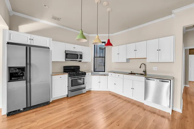 a kitchen with stainless steel appliances granite countertop a refrigerator a sink dishwasher a stove and white cabinets with wooden floor