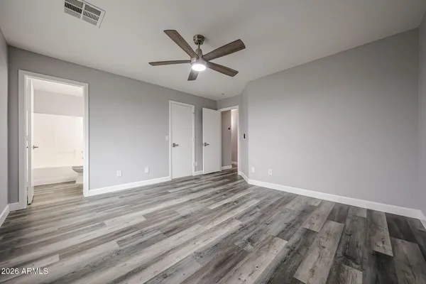 a view of an empty room with wooden floor and a ceiling fan