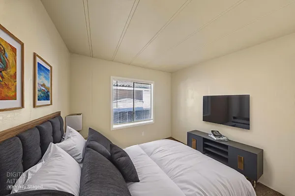 a bedroom with a bed television on desk and a window