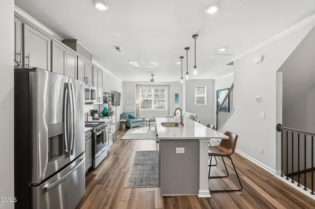 a kitchen with stainless steel appliances a refrigerator a stove a sink dishwasher and a dining table with wooden floor