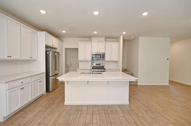 a large kitchen with stainless steel appliances granite countertop a stove top oven a refrigerator and white cabinets with wooden floor