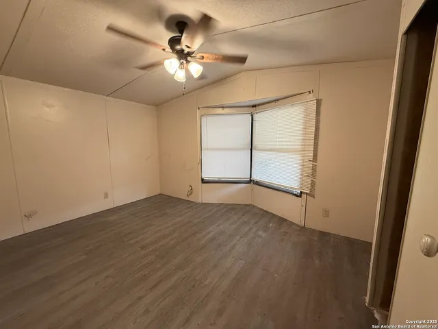 an empty room with wooden floor fan and windows