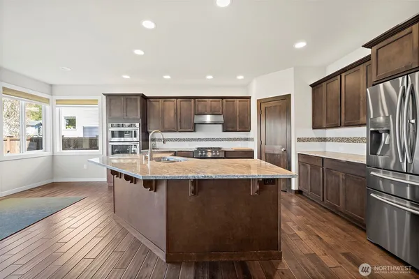 a large kitchen with stainless steel appliances kitchen island granite countertop a stove a refrigerator a sink a dining table and chairs with wooden floor