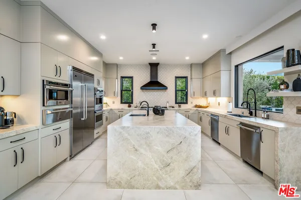 a large white kitchen with stainless steel appliances granite countertop a stove top oven a sink dishwasher a dining table and chairs with wooden floor