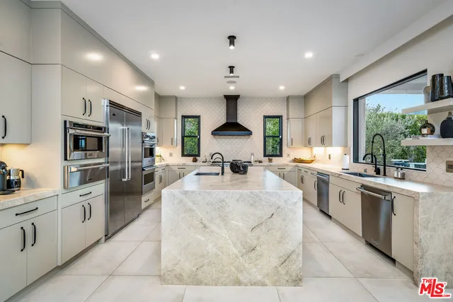 a large white kitchen with stainless steel appliances granite countertop a stove top oven a sink dishwasher a dining table and chairs with wooden floor