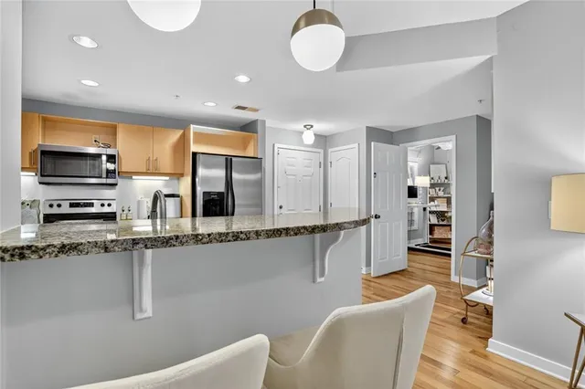 a kitchen with stainless steel appliances granite countertop a stove top oven a sink a dining table and chairs with wooden floor