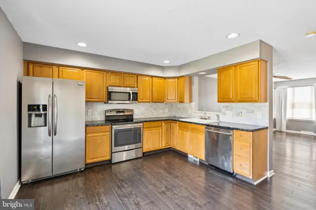 a kitchen with stainless steel appliances granite countertop a refrigerator a sink dishwasher a stove and a sink with wooden floor