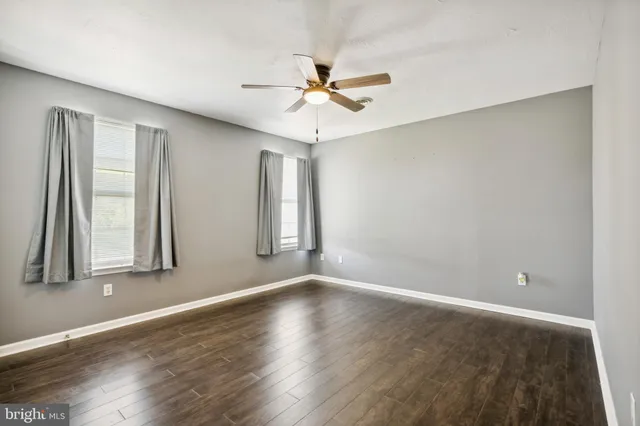 an empty room with wooden floor fan and windows
