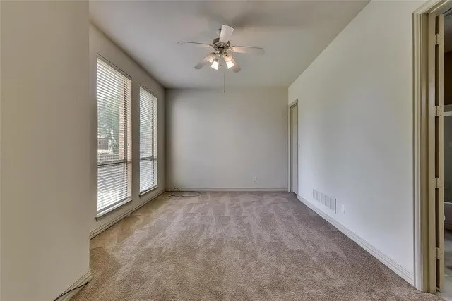 an empty room with chandelier fan and windows