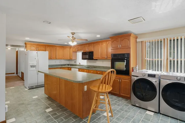 a kitchen with stainless steel appliances granite countertop a sink a stove a refrigerator cabinets and chairs