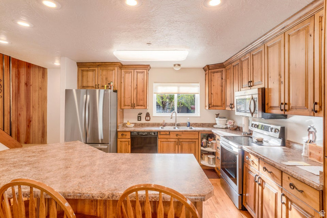 48 South Sage Road Pine Valley, UT 84781 - Photo 18 of 61 Kitchen featuring wood-finish cabinetry, stainless steel appliances, a composite countertop, an island with breakfast bar seating, and a stainless steel sink with a single-handle faucet