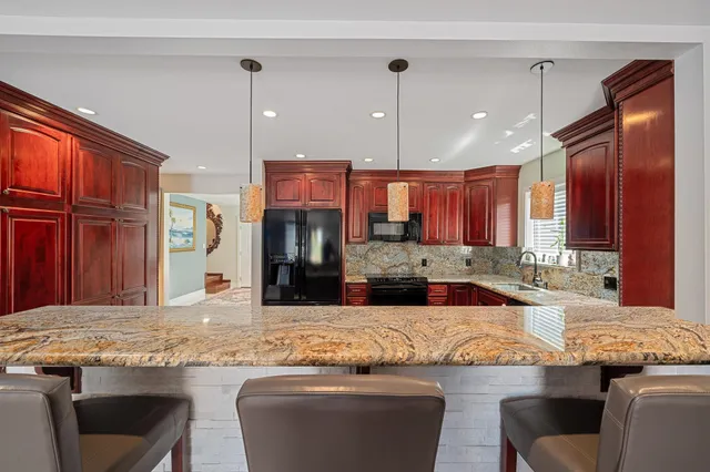 a kitchen with granite countertop a stove a sink a refrigerator and chairs