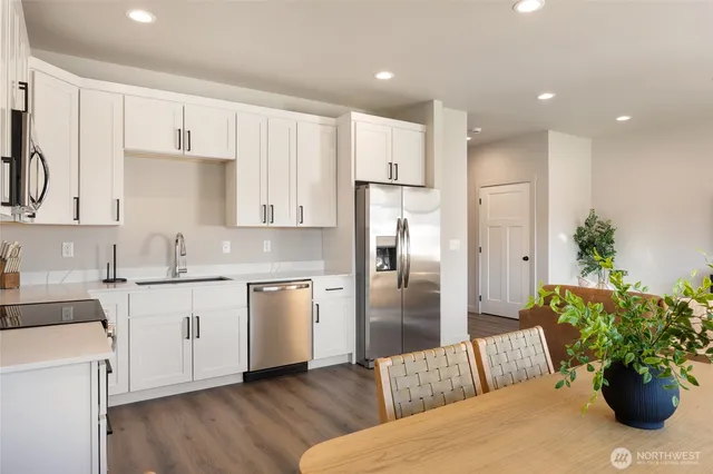a kitchen with stainless steel appliances kitchen island granite countertop a refrigerator a sink dishwasher and white cabinets with wooden floor