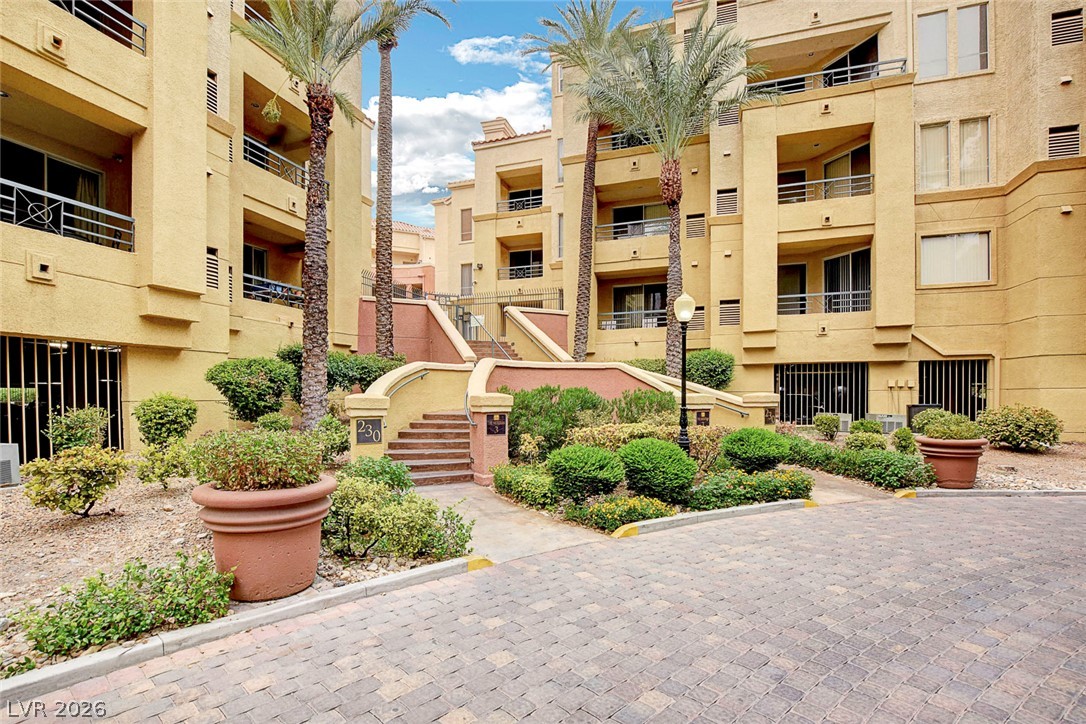 230 East Flamingo Road, Unit 106 Las Vegas, NV 89169 - Photo 29 of 66 Mature palm trees and lush shrubs frame this multi-story residence with an inviting brick paver driveway.
