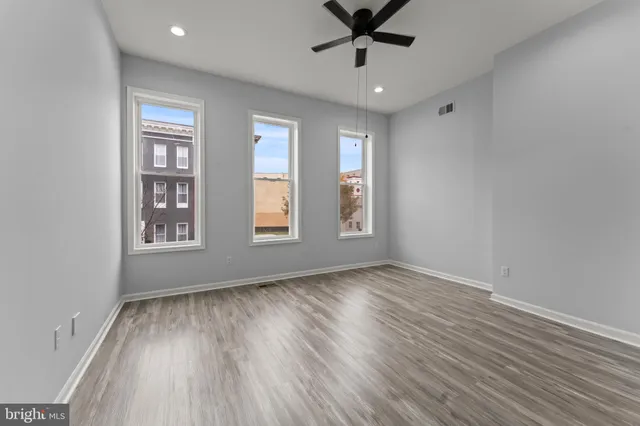 a view of empty room with wooden floor and fan