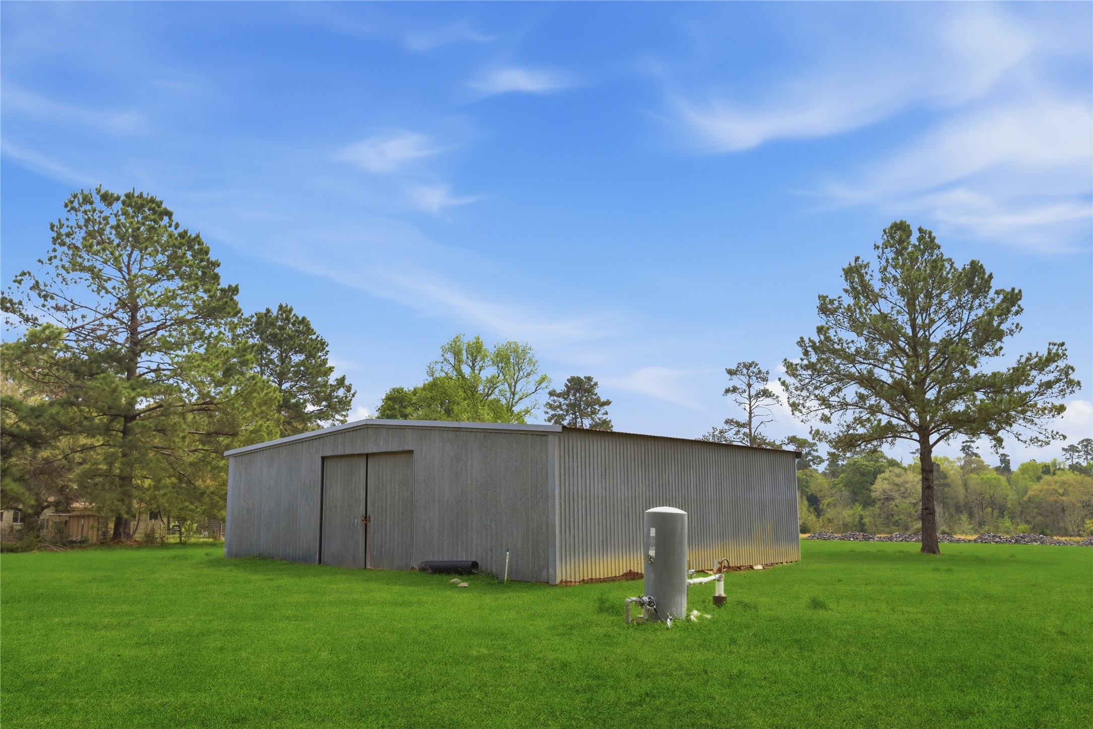 872 Four Notch Road Huntsville, TX 77340 - Photo 9 of 42 Spacious metal storage building set on lush green grounds, surrounded by mature trees, offering ample space for various uses.