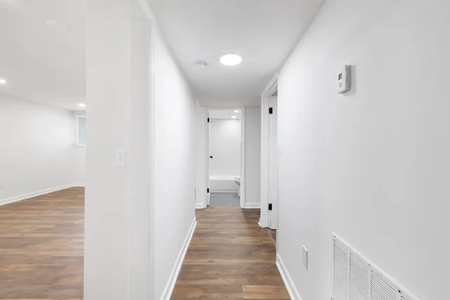 a view of a hallway with wooden floor and a bathroom