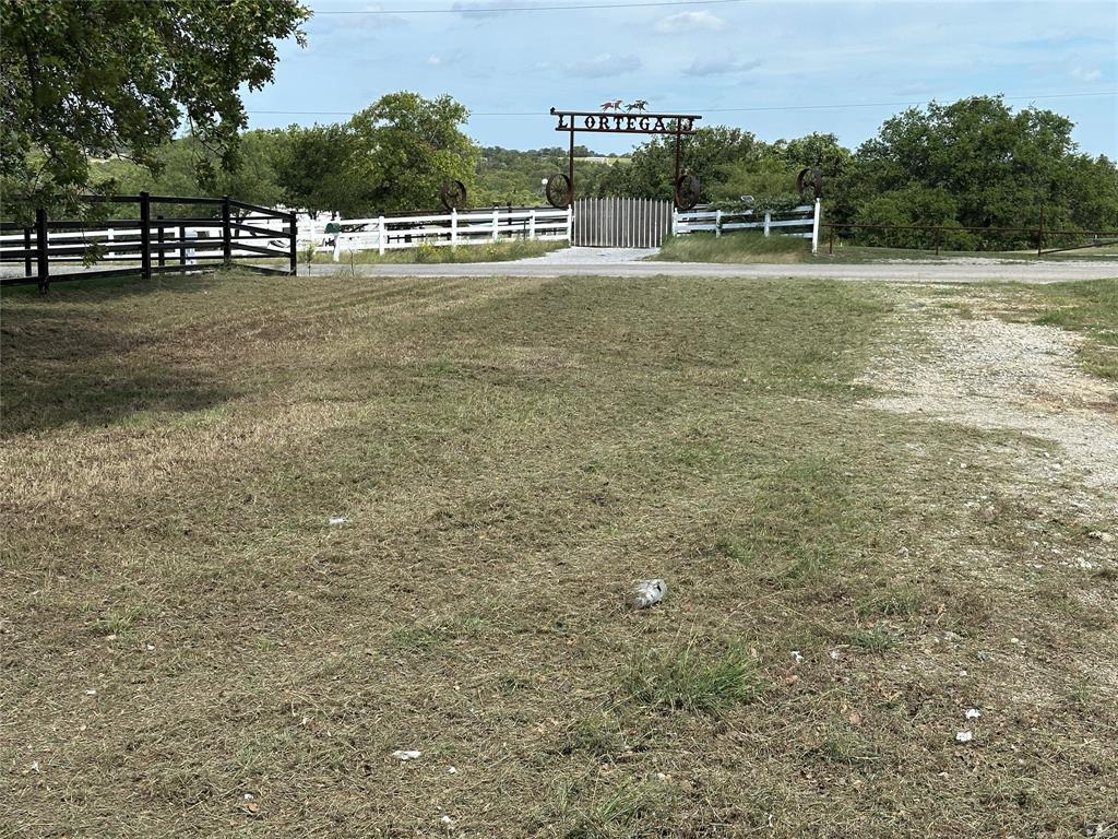 570 Big Salty Lane Springtown, TX 76082 - Photo 8 of 36 Gated entrance featuring a decorative metal archway, white perimeter fencing, and established trees